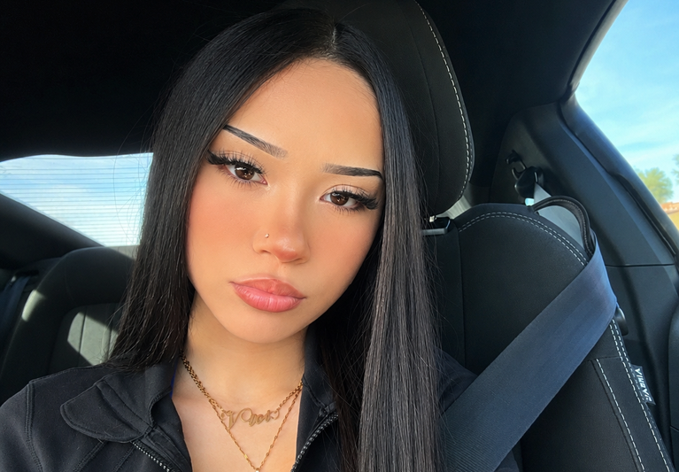 vivi2freaky car selfie portrait showcasing her long straight black hair, winged eyeliner, nose piercing, and signature gold script name necklace.